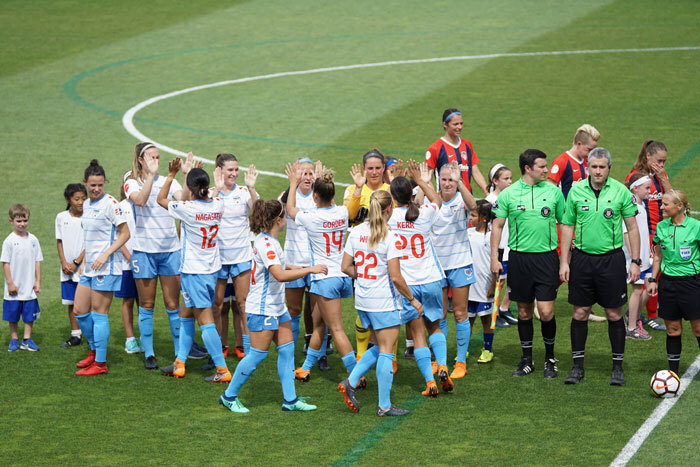 Women’s football team on the field celebrating before a match, with referees standing nearby.