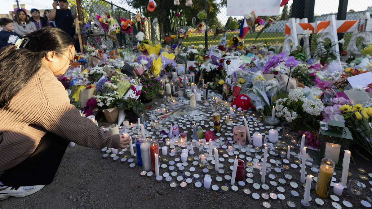 Woman lighting a candle at a vigil with flowers and candles honoring victims of Vancouver festival attack aftermath.