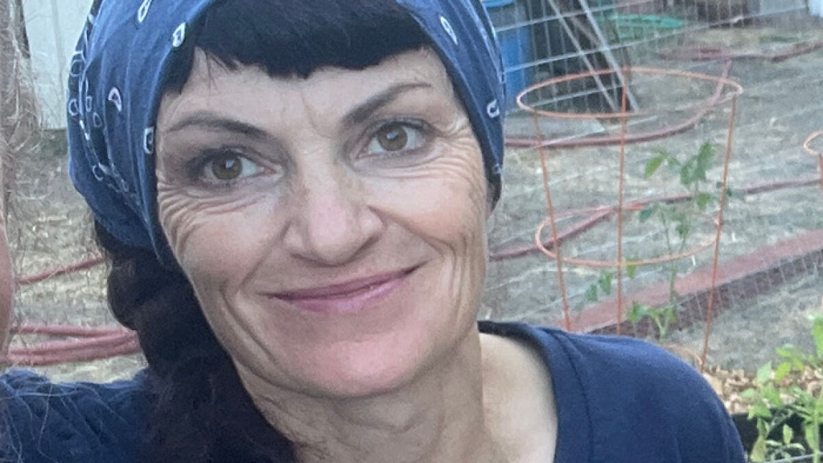 Irish woman with a blue headscarf smiling outdoors near garden plants, highlighting legal status and potential ICE detention concerns