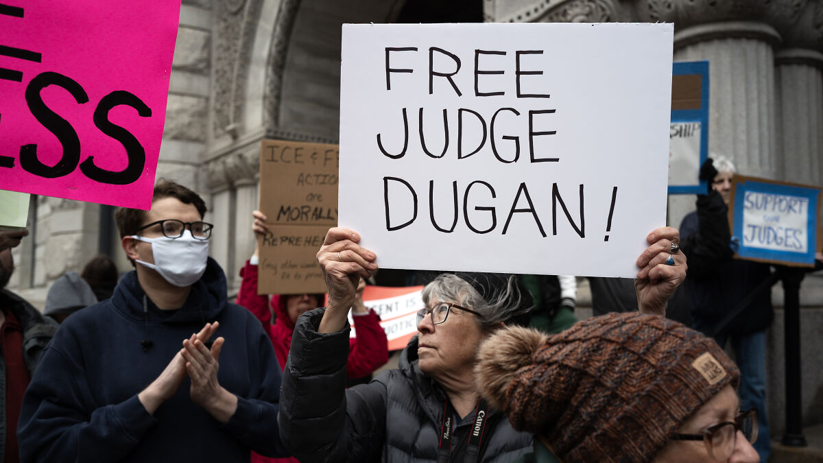 Protesters holding signs supporting judge Dugan amid suspension allegations of helping defendant evade ICE agents.