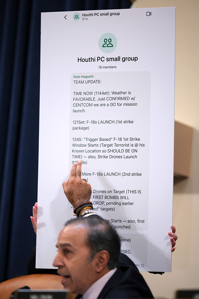 Man points to Pete Hegseth's messages on a chat screen about war plans in a group discussion.