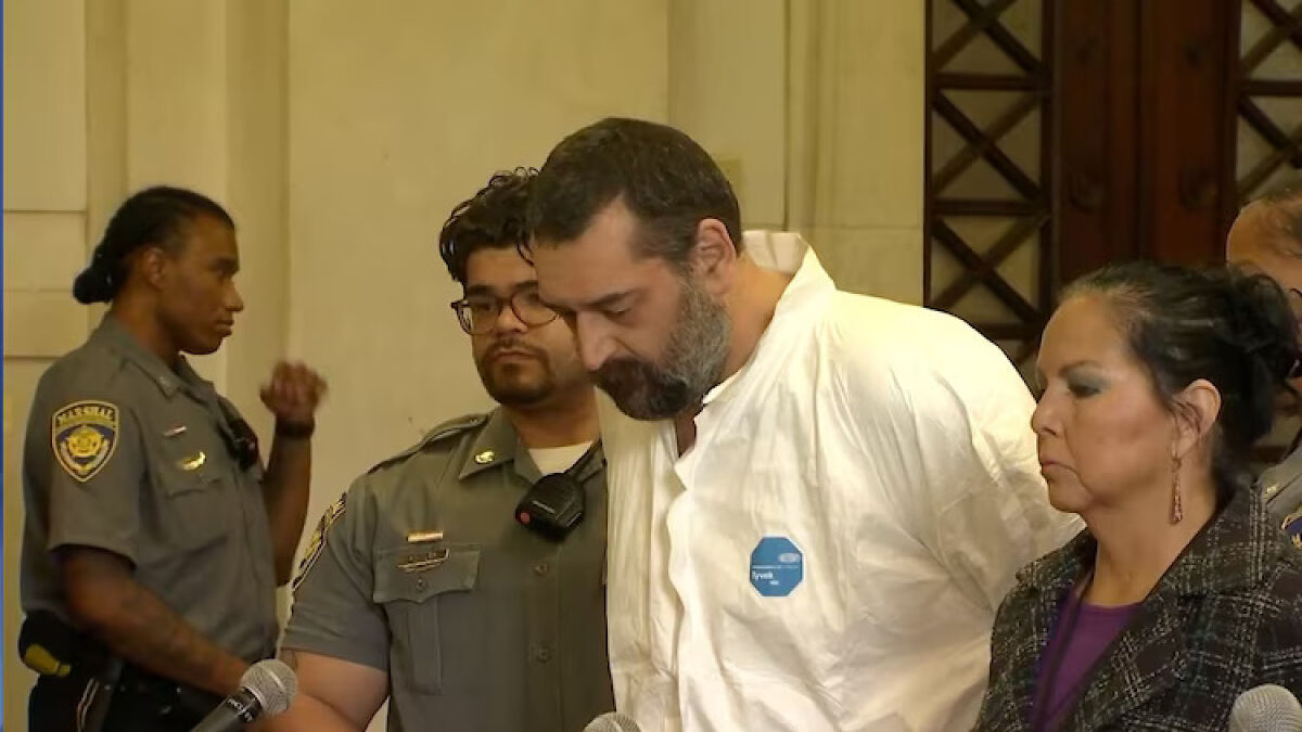 Man allegedly beat 12-year-old son to death with baseball bat, shown escorted by police in a courtroom setting.