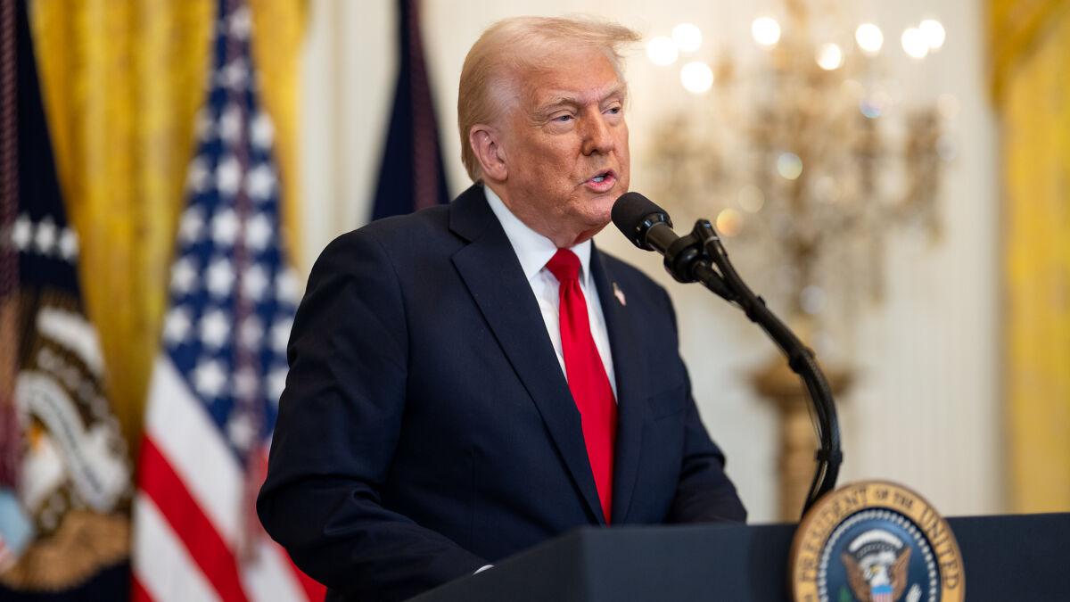 Donald Trump speaking at a podium with US flags in the background, related to Harvard witch hunt targeting international students.