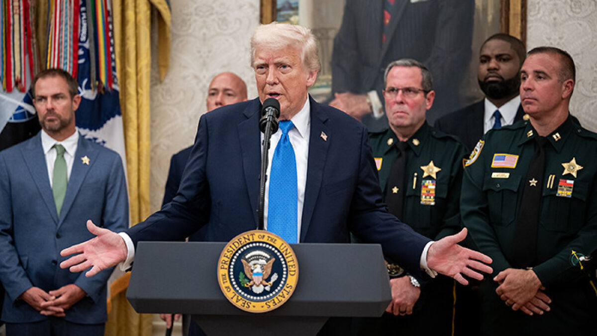 Donald Trump speaking at a podium with presidential seal, surrounded by law enforcement officials and aides.