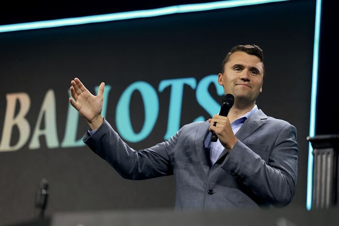 Conservative pundit speaking on stage with microphone in hand, addressing audience during a public event.