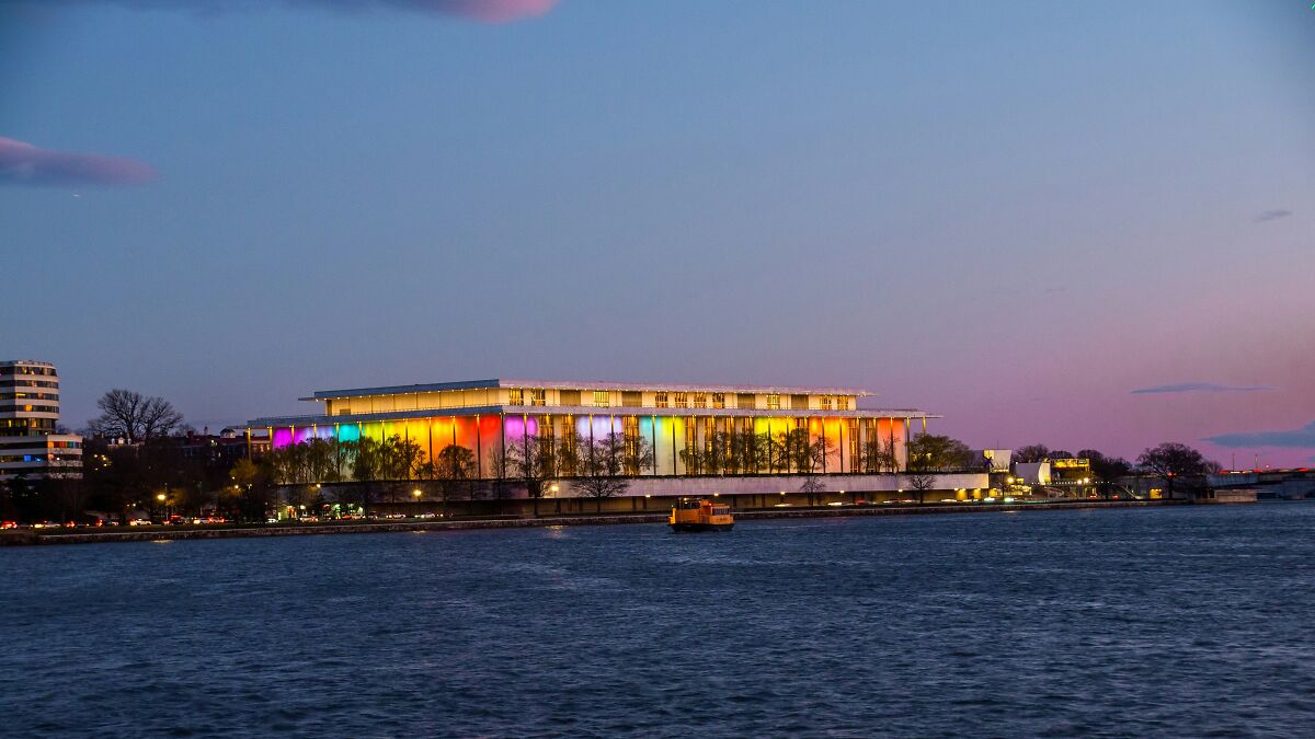 Kennedy Center at dusk with colorful lights along the waterfront symbolizing arts institution earnings decline.