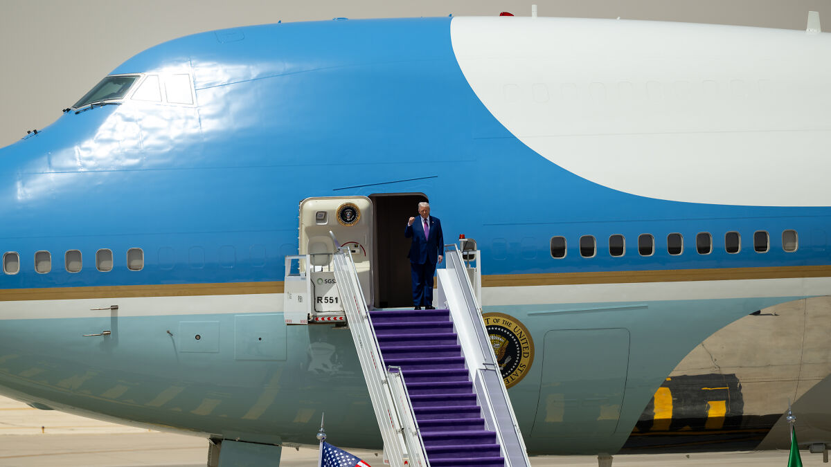 Donald Trump standing on Air Force One steps, wearing a suit, moments before stumbling while descending the stairs.