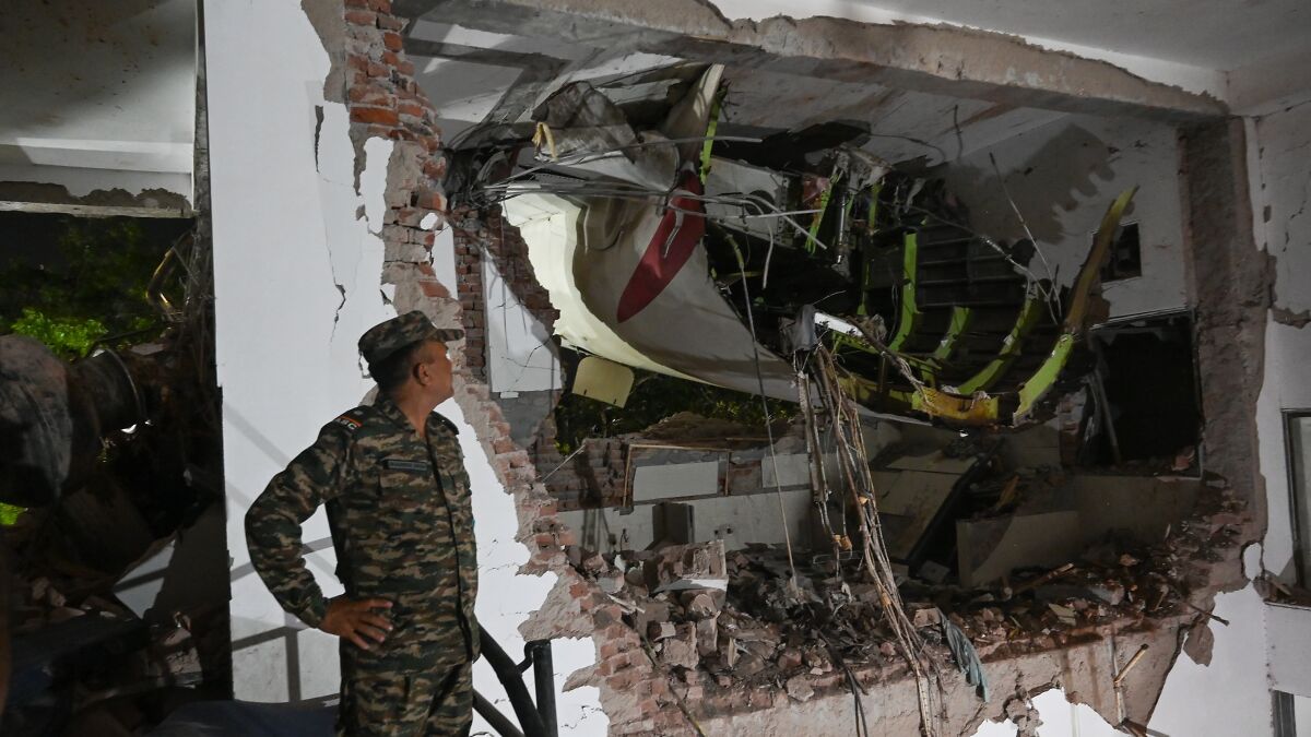 Military personnel inspecting Air India crash wreckage inside a damaged building at the crash site during night hours.