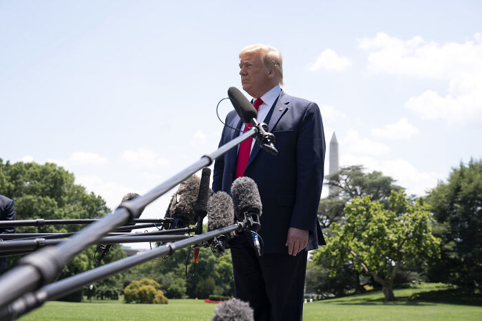 Former President Trump speaking outdoors in a suit near microphones about immigrant families and fear of separation impacting self-deport decisions.