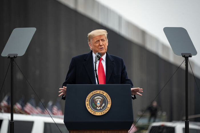 Former President Donald Trump speaking at a podium with presidential seal near a border wall, related to agriculture secretary and farmworkers. Former President Donald Trump speaking at a podium with presidential seal near a border wall, related to agriculture secretary and farmworkers.