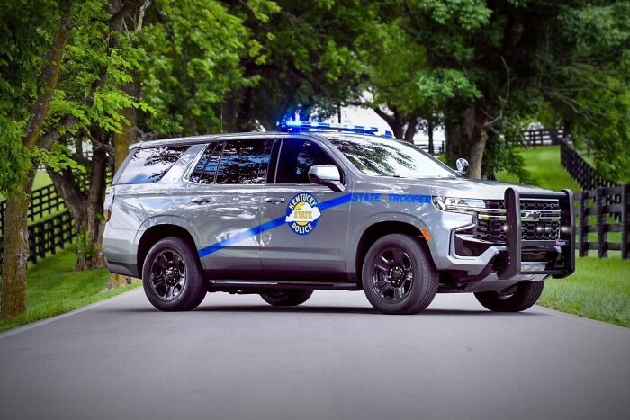 Kentucky State Police vehicle with flashing lights on a rural road near trees responding to shootings incident.