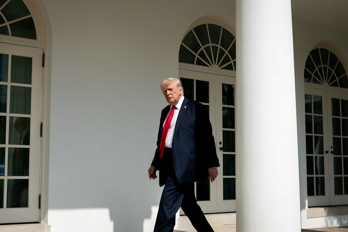 Man in a dark suit and red tie walking outside a white building, related to Josh Hawley and Medicaid cuts legislation.