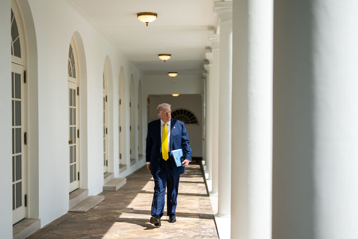 Man walking in columned hallway holding documents, concept related to MAGA voter and child trafficking charges.