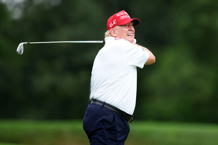 Man wearing a red hat and white shirt swinging a golf club, viral golf video alleges cheating at Turnberry.