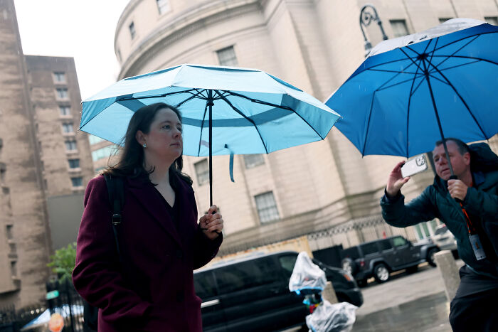Woman holding blue umbrella outside courthouse during high-profile DOJ prosecution related to James Comey’s daughter.