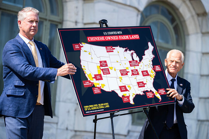 Two men hold a map showing counties with Chinese owned farm land amid agriculture and farmworker policy discussion. Two men hold a map showing counties with Chinese owned farm land amid agriculture and farmworker policy discussion.
