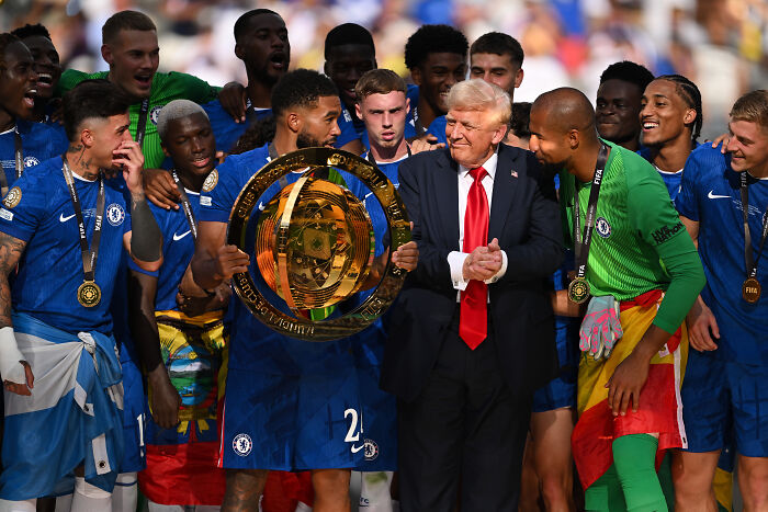 Chelsea players holding Club World Cup trophy next to Trump during trophy presentation as crowd boos at the event.
