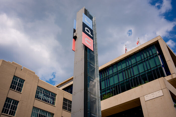 NPR building exterior with a tall logo tower under a partly cloudy sky, related to Trump’s quest to sue and silence critics.