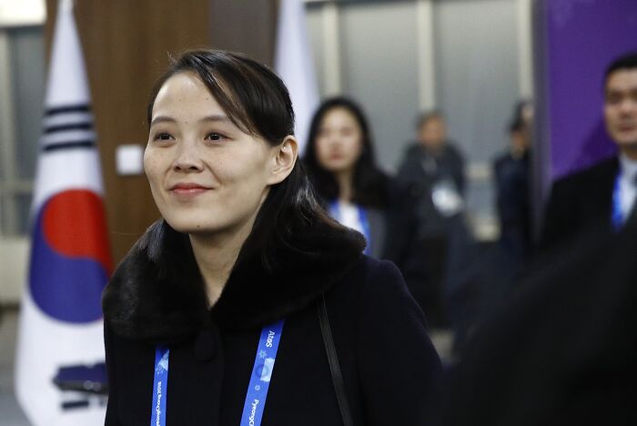 Kim Jong Un’s sister in a black coat attending an event with the South Korean flag in the background.