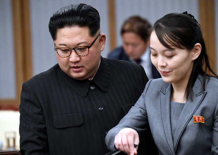 Kim Jong Un’s sister in a grey suit with a pin, engaging with Kim Jong Un in black, rejecting South Korea dialogue efforts.
