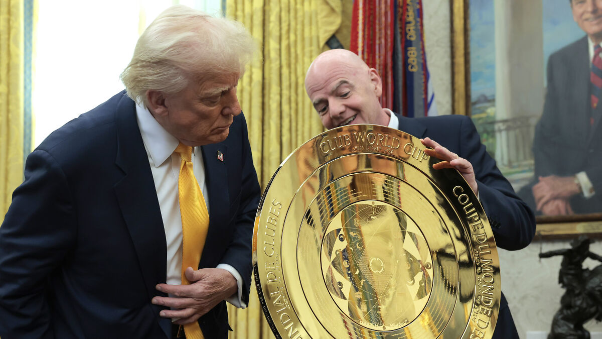 Donald Trump and FIFA president examining the gold Club World Cup trophy in an indoor setting with framed portraits.