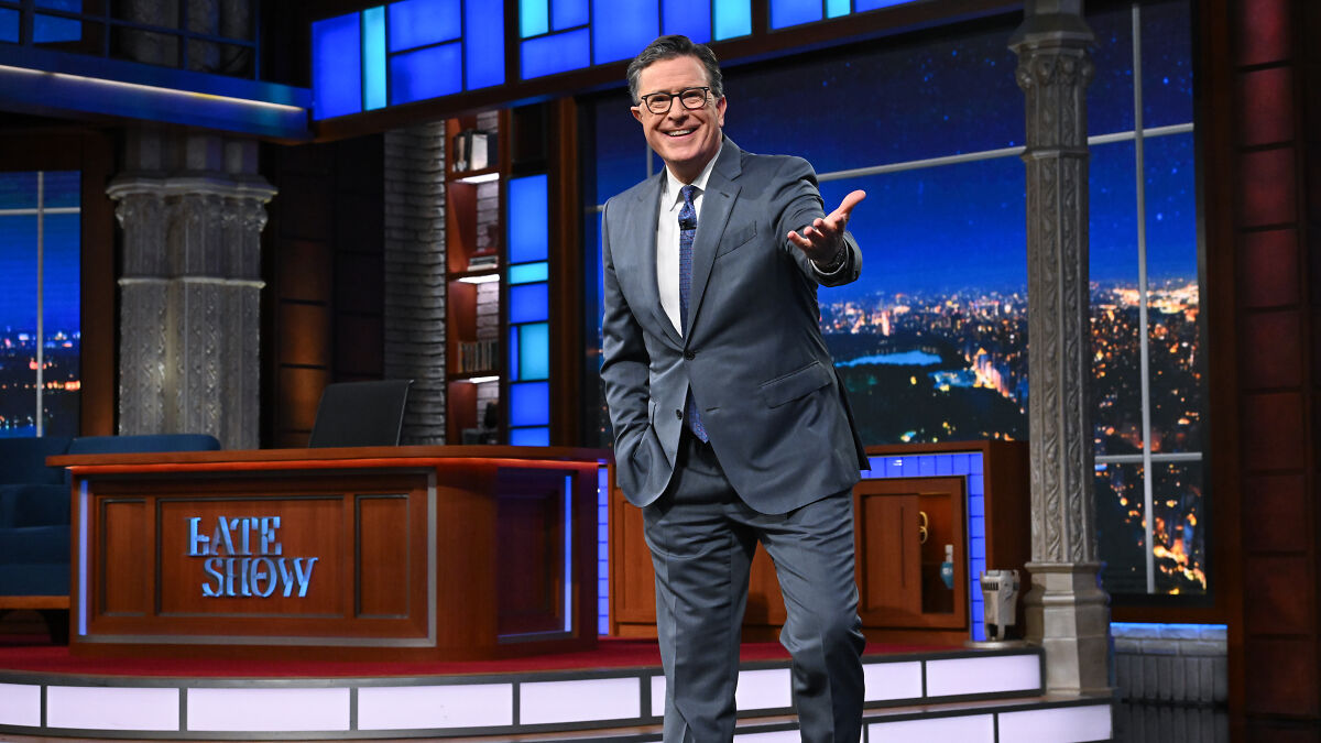 Stephen Colbert on Late Show stage, wearing suit and glasses, smiling and gesturing amid Stephen Colbert show canceled news.