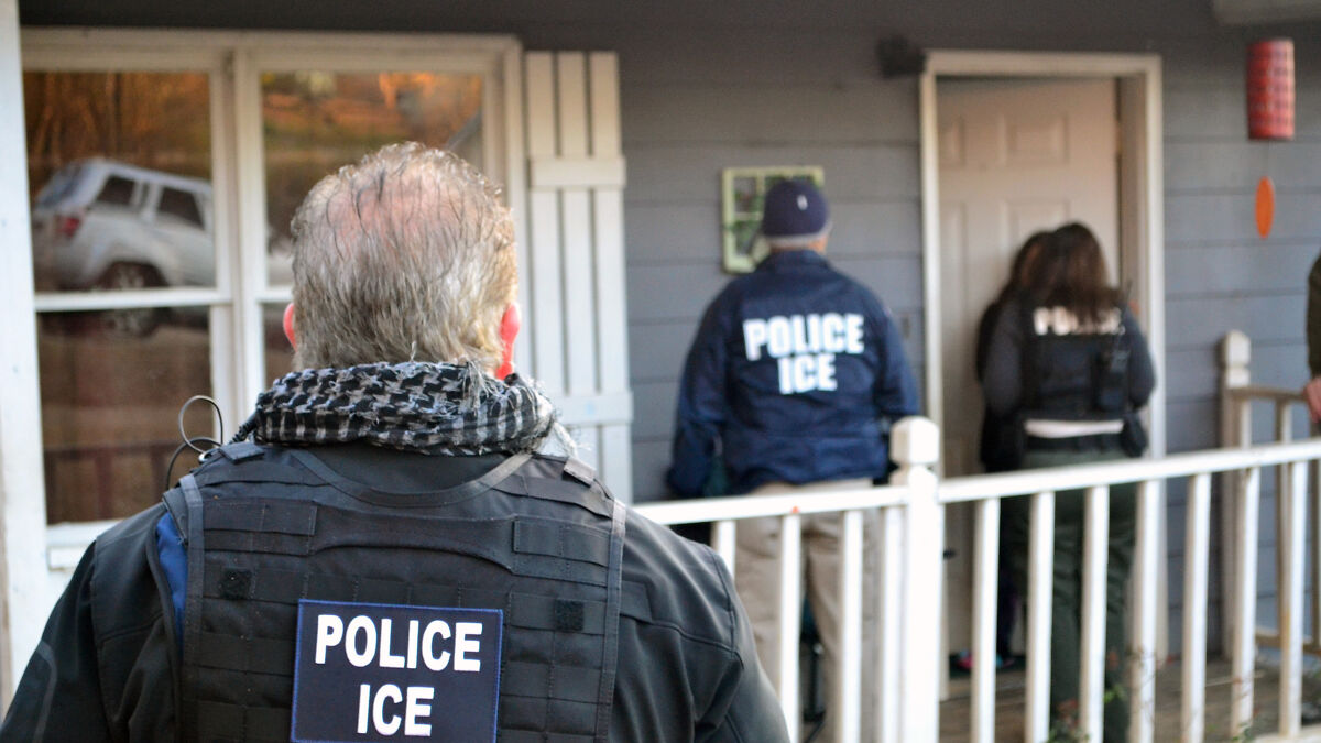Three police ICE officers wearing jackets stand outside a house, highlighting concerns about Medicaid records access.