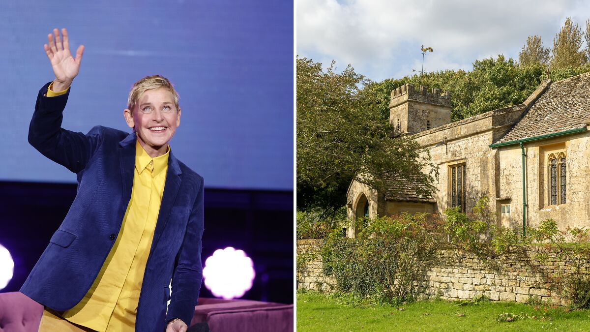 Ellen DeGeneres waving on stage in a yellow shirt and blue jacket beside a stone home with greenery under a cloudy sky