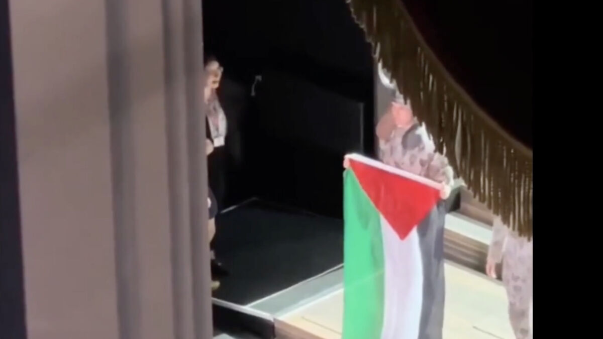 Performer unfolding a Palestinian flag onstage at Royal Opera House amid chaotic scene during the event.