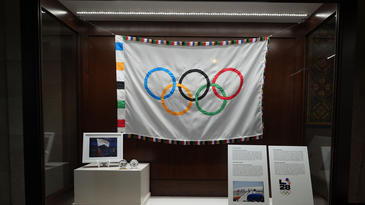 Olympic flag displayed in a glass case with informational plaques, representing U.S. Olympic Committee transgender athlete ban.