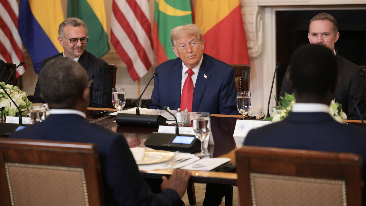 Former President Trump at a meeting table discussing immigration and asylum seekers with officials in a formal setting.