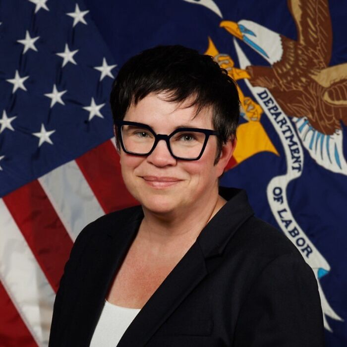 Labor statistics chief posing in front of American and Department of Labor flags, linked to weak jobs report controversy.