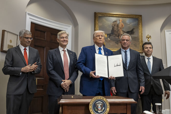 Donald Trump holding signed document with Big Pharma executives in a formal room, highlighting drug pricing discussions.