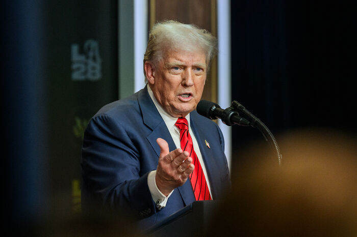 Man in suit and red tie speaking at a podium with microphone, related to mortgage fraud investigation keywords.