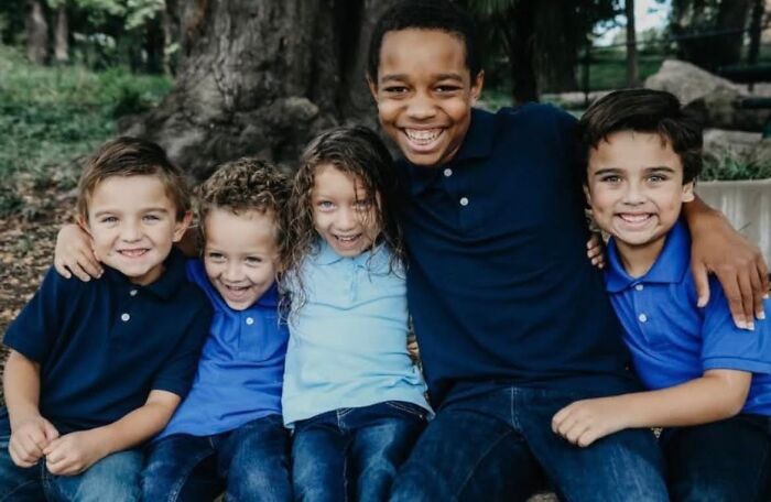 Group of smiling children sitting outdoors, illustrating family connection related to Giovanni Pelletier’s story.