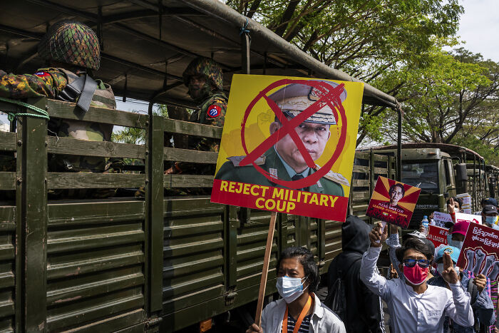 Protesters in Myanmar hold signs against military coup as junta moves forward with sham election amid atrocity allegations.