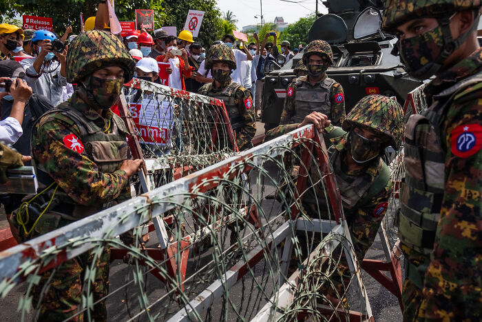 Myanmar’s junta soldiers blocking protesters with barbed wire during tensions amid sham election allegations.