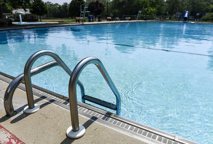 Empty swimming pool with metal ladder in focus on a sunny day symbolizing a 9-year-old girl’s courageous move after attack