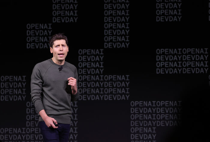 Man speaking on stage with OpenAI DevDay text in background highlighting dangers of relying on AI therapists for teens.
