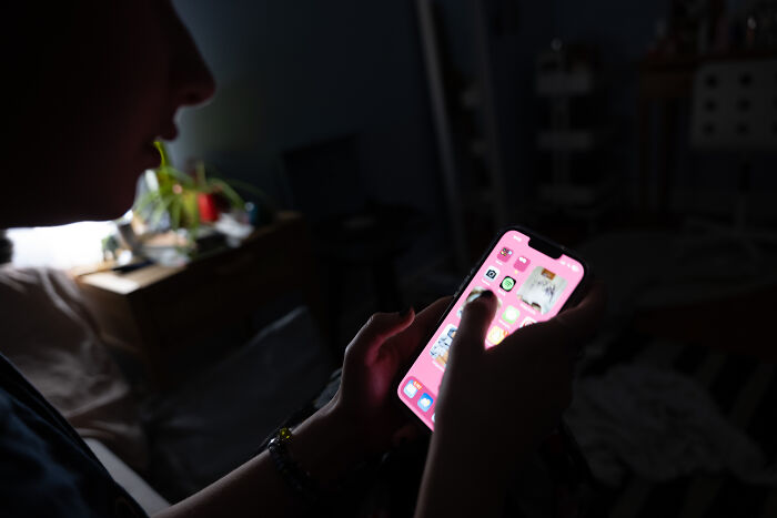 Person using smartphone in dark room highlighting concerns about latest streamer tragedy and toxic online challenges debate