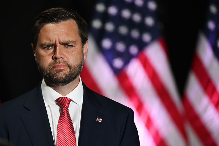 J.D. Vance speaking at an event with American flags in the background, related to river water level raise.