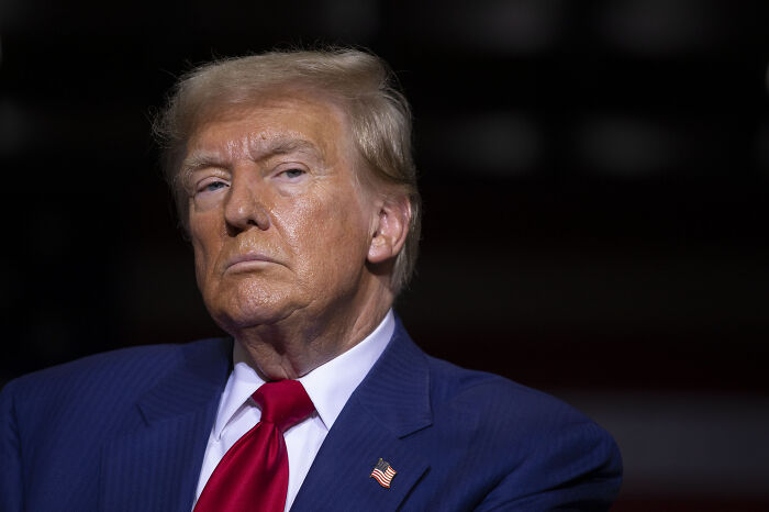 Close-up of a serious man in a blue suit with a red tie, relating to FBI raids and a major national security investigation.