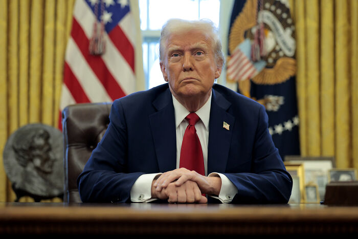 Former President Donald Trump sitting at the Resolute Desk in the Oval Office, symbolizing lessons to avoid World War III.