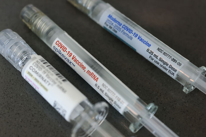 Syringes labeled mRNA COVID-19 vaccine doses on a dark surface representing mRNA vaccine development funding cuts