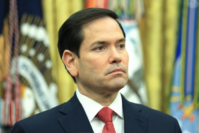Man in suit and red tie in official setting, representing foreign tourists required to pay for U.S. visa in pilot program