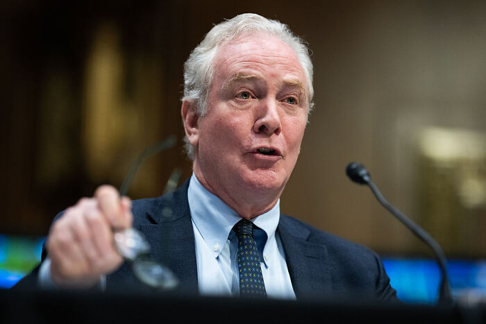 Man speaking at a hearing, raising glasses, illustrating question over FBI’s legal right in Texas redistricting standoff.