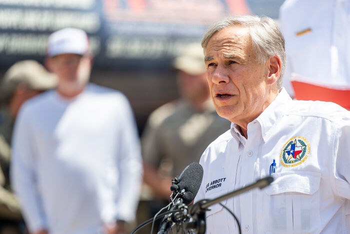 Texas Governor Greg Abbott speaking at a podium amid questions over FBI’s legal right to chase Texas lawmakers.