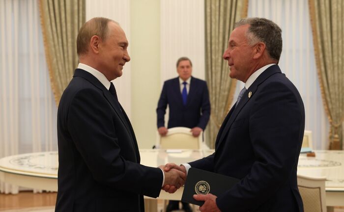Vladimir Putin shaking hands with a man in a suit during a formal meeting discussing Ukraine occupation in a government setting.