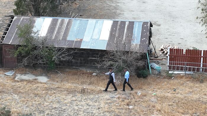 Two men walking near a weathered shed in dry grass, related to Emmanuel Haro’s dad confession report.