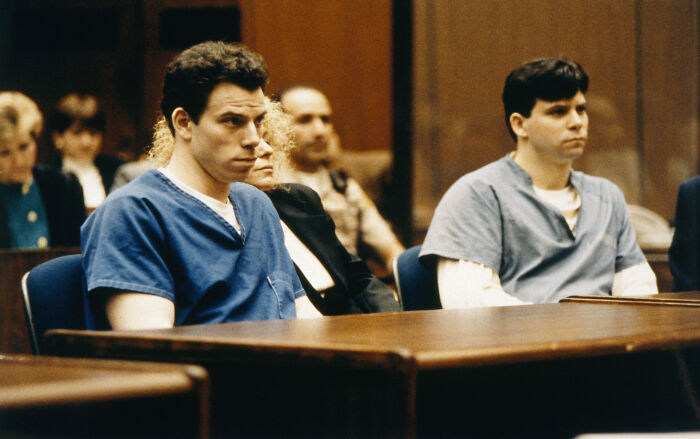 Erik Menendez in court with his brother, both wearing prison uniforms during a legal proceeding related to parole denial.